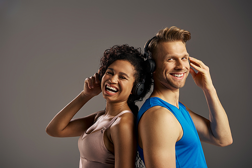 A young man and woman in activewear are immersed in music, listening through headphones with expressions of joy and connection.