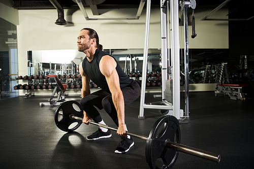 A focused man in active wear performs a squat with a barbell in a gym, showcasing strength and determination.