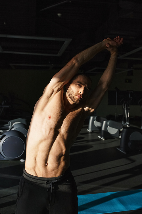 A muscular man without shirt holding his arms up in triumph at the gym.