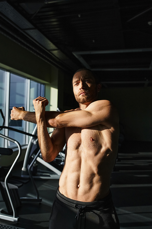 A shirtless muscular man flexes his muscles in a gym, showcasing his strength and physical prowess.