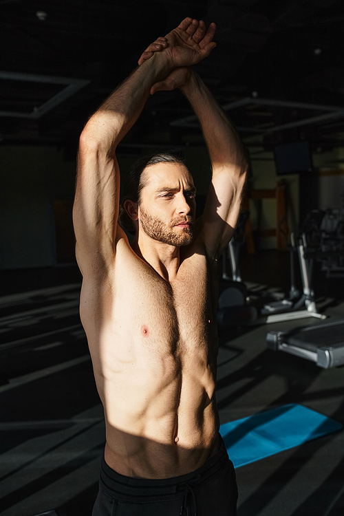 Muscular shirtless man standing in gym with hands up, showcasing strength and determination in workout session.