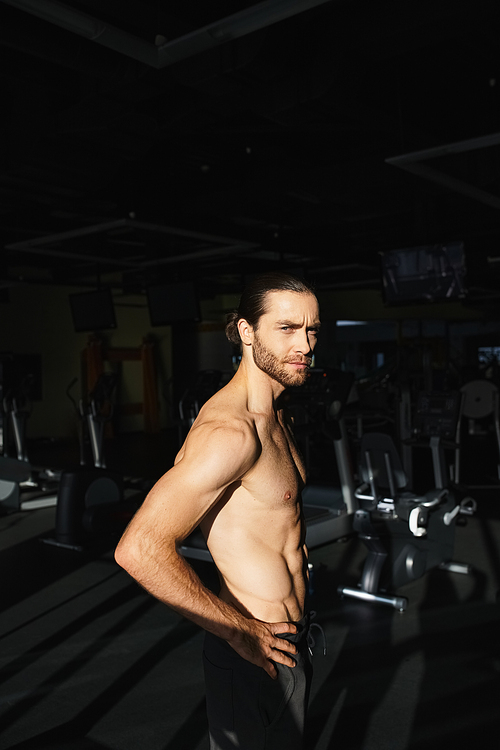 A shirtless muscular man showcasing his strength while standing in a gym setting.