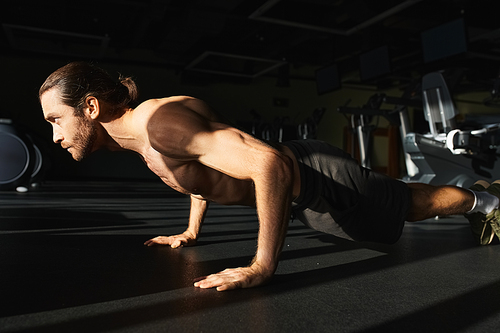 Muscular shirtless man doing push ups in a gym.