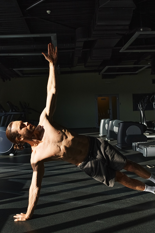 Muscular man, shirtless, showcasing strength and balance by performing a handstand in a gym setting.