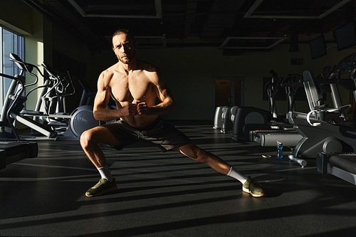 Muscular man without shirt doing a squat exercise in a gym with determination and focus.