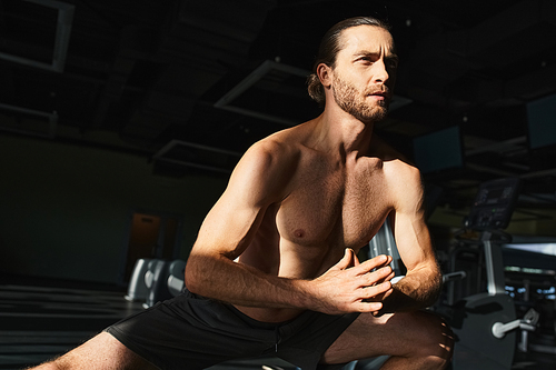 A muscular man bare-chested, squatting on a bench in a gym, showcasing strength and dedication to fitness.