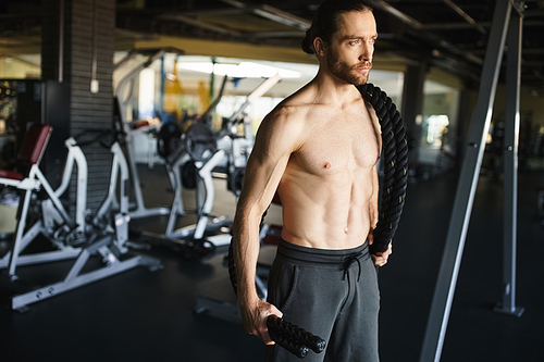 A muscular man stands confidently in a gym, focused on his workout routine, showcasing his dedication to building strength.