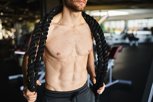 A muscular man without a shirt fiercely holds a rope, showcasing his strength and determination during a workout session in the gym.