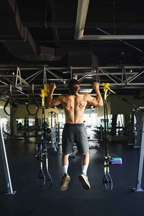 Muscular man without shirt doing pull ups on a bar in a gym.