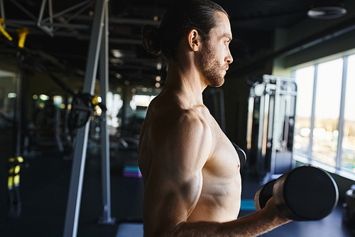 A shirtless man flexing his muscles while holding a dumbbell in a gym, showing dedication to his workout routine.