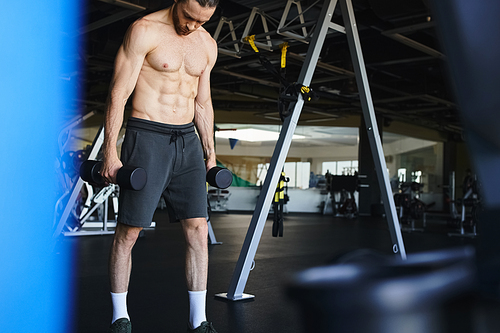 A shirtless, muscular man lifts a dumbbells in a gym, showcasing strength and commitment to his workout routine.