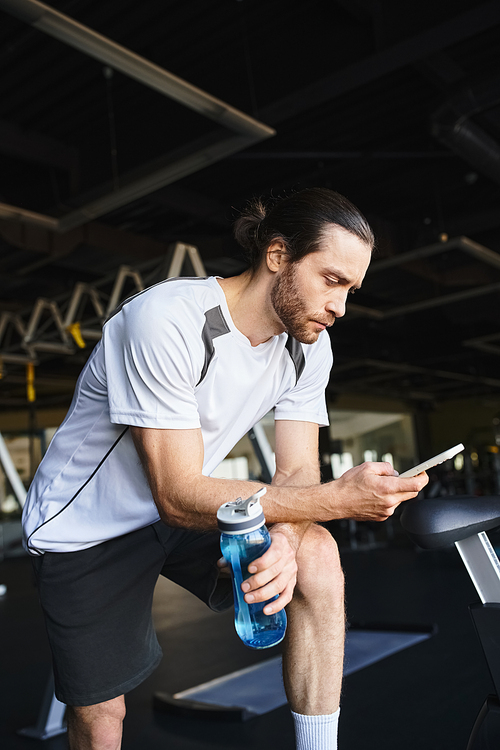 A muscular man sitting on a bench, absorbed in his cell phone.