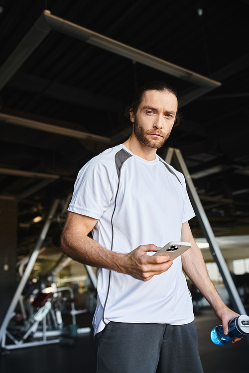 A man in a white shirt engaged in his smartphone after workout in gym