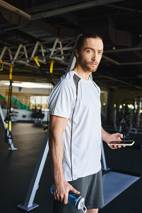 A muscular man hydrating with a water bottle in a gym while working out.