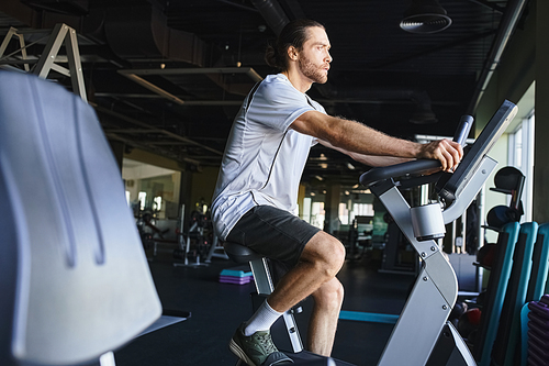 A muscular man is energetically cycling on a stationary bike at the gym.