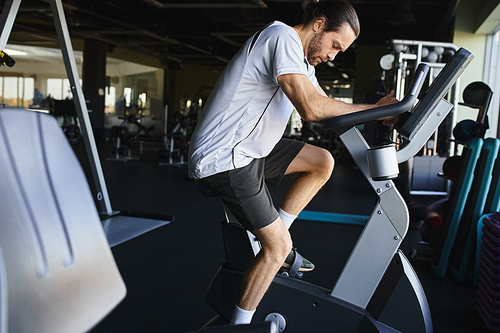 A muscular man is cycling on a stationary bike in a gym, focused and determined.