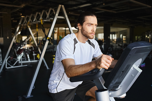 A muscular man working out on a stationary bike in a gym, focusing on improving his fitness and endurance.