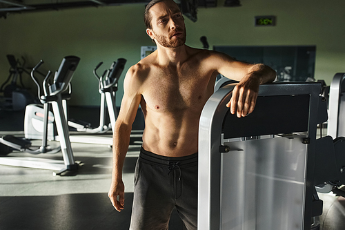 Muscular man works out next to large machine in gym.