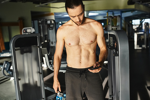 A muscular man holding a phone in a gym, using social media after workout