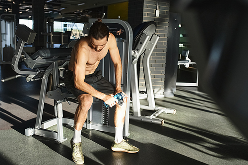 Muscular man sitting on gym bench, taking a break from workout, deep in thought.