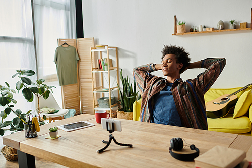 Young African American male blogger sitting at desk, hands on head, deep in thought.