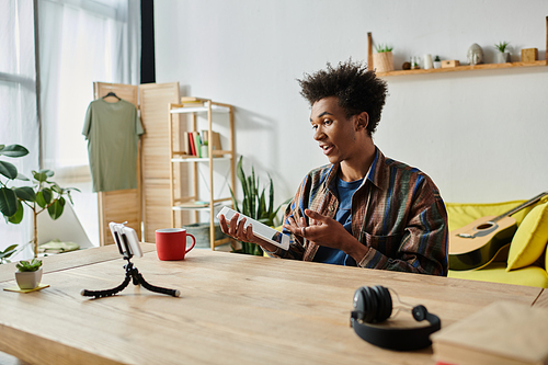 Young man, African American, blogs on phone camera at table.