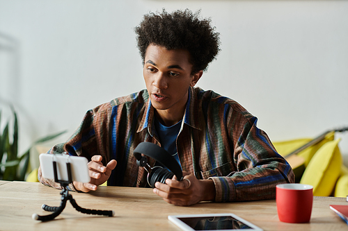 A young African American man sits at a table, engaging with a phone and tripod while talking.