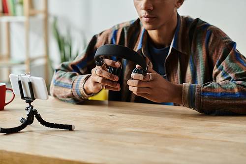 A young African American male blogger simultaneously holds a phone and a headset.