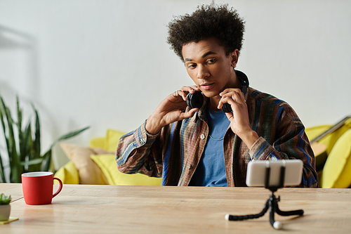 A young African American blogger sits at a table, savoring a cup of coffee while speaking into his phone camera.