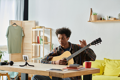 A young man, playing an acoustic guitar, creates music in his cozy living room.