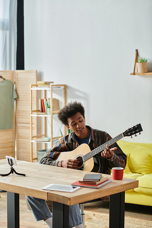 A man of African American descent sits at a table, engrossed in playing an acoustic guitar.