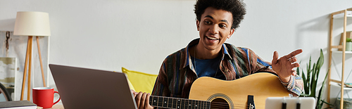 A young man playing acoustic guitar in front of a phone while immersed in music.