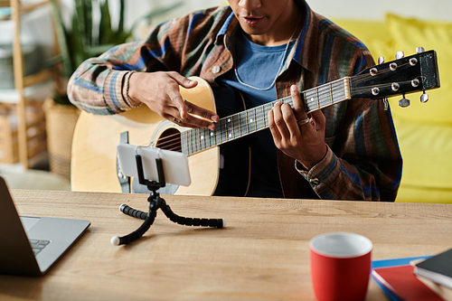 Young African American male blogger plays guitar while speaking on phone camera.