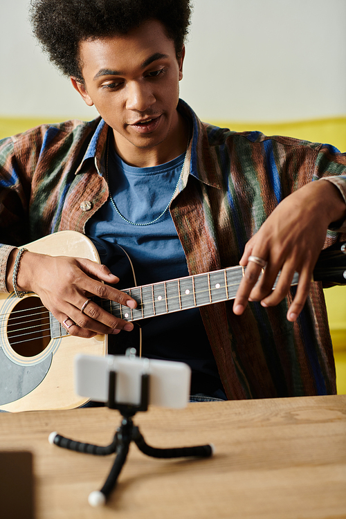 A young man creates beautiful music, playing an acoustic guitar in front of a phone.