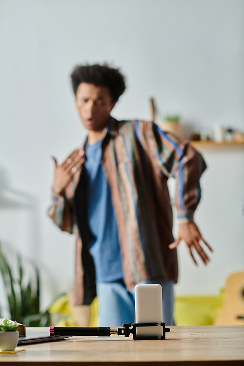 A young African American male blogger is standing in front of a table, talking on his phone camera.