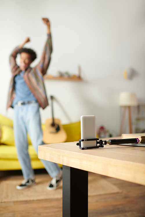 Young African American man dancing energetically on a yellow couch in a lively living room.