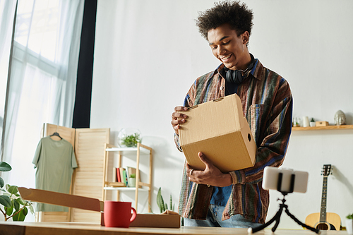 A young Black man displays a cardboard box in front of a desk.