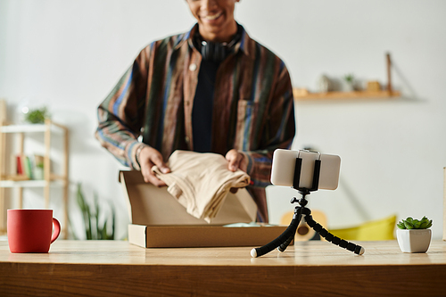 A young African American male blogger opens a box while talking on the phone camera.