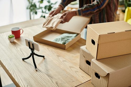 A young African American male blogger talks on the phone while placing boxes on a table.