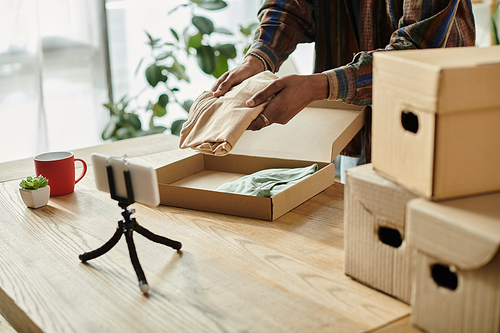 Young African American male blogger talking on phone camera while putting boxes on a table.