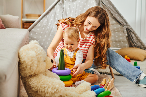 A young mother and her toddler daughter happily playing with a teddy bear, creating heartwarming memories at home.