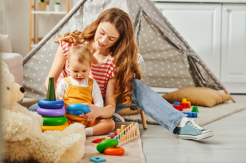 A young mother happily playing and interacting with her toddler daughter in the comfort of their home.