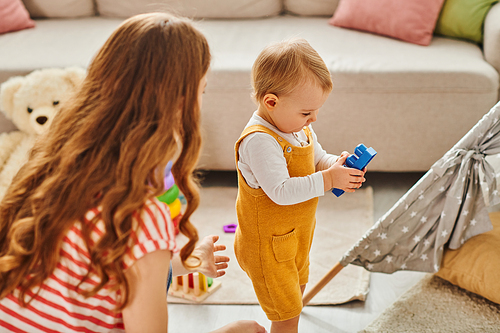 A young child, accompanied by her mother, gleefully explores the living room with a colorful toy.