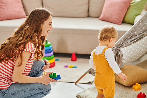 A young mother joyfully engages with her toddler daughter in cheerful play in a cozy living room setting.