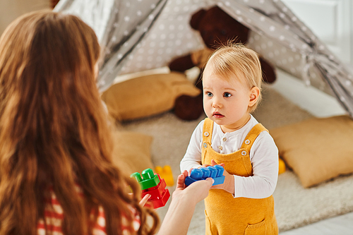 A young mother happily engages with her toddler daughter, playing together in a cozy room filled with love and joy.