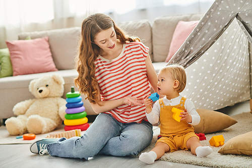 A young girl sits on the floor, engrossed in play with a toddler, sharing joyful moments in a home setting.