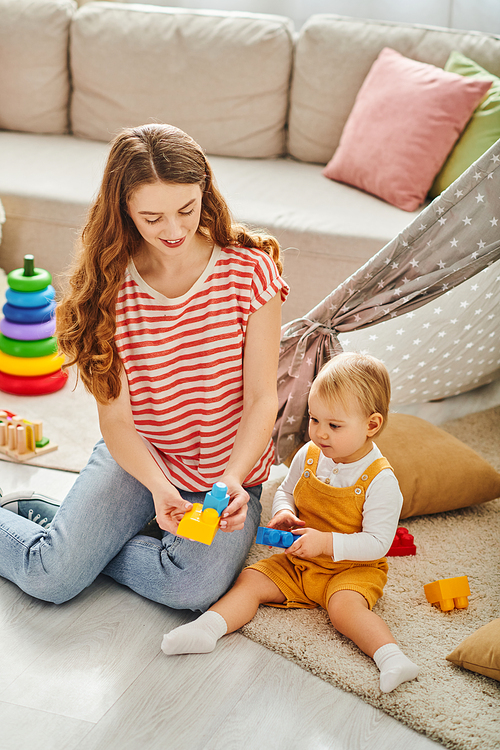 A young mother sitting on the floor, joyfully engaging with her toddler daughter through play and interaction.