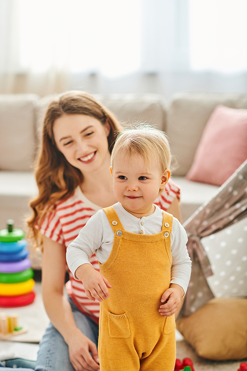 A young woman sits peacefully beside her toddler daughter in a cozy living room, sharing a moment of tender connection.