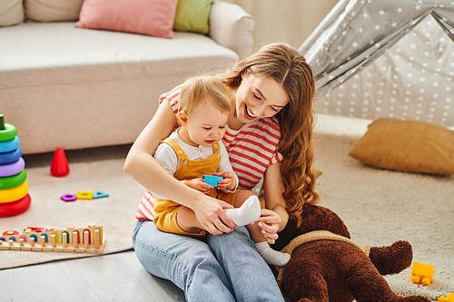 A young mother sits on the floor, playing with her toddler daughter in a heartwarming moment of bonding and joy.