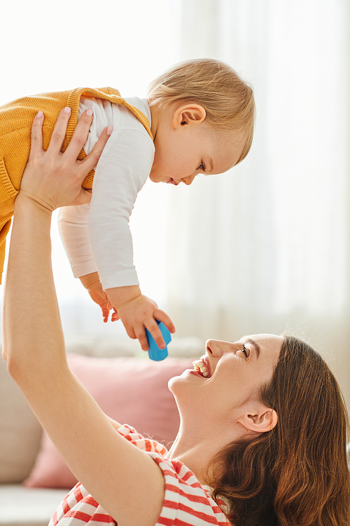 A woman joyfully lifts her toddler daughter high in the air as they bond and enjoy quality time together at home.